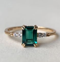 an emerald and diamond ring on a white surface