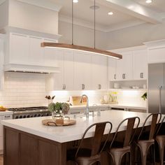 a large kitchen with white cabinets and an island that has chairs around it in front of the counter