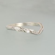 a silver ring with two leaves on the top and one leaf on the bottom, sitting on a gray surface