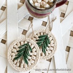 two crocheted christmas ornaments on a table next to a cup of hot cocoa