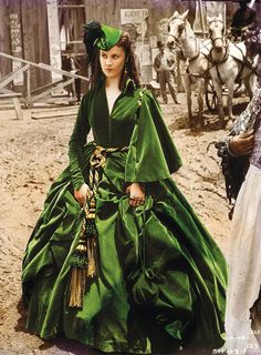 a woman in a green dress standing next to a man with a horse behind her