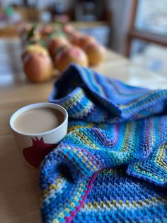 a cup of coffee sitting on top of a table next to a blanket and fruit