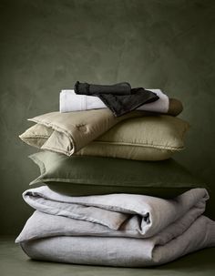 folded linens and pillows stacked on top of each other in different colors, sizes and shapes