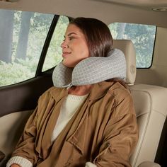 a woman sitting in the back seat of a car with a neck pillow on her head