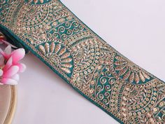 a close up of a green and gold ribbon on a white surface with flowers in the background