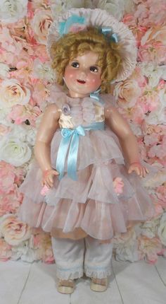 a doll is standing in front of a flowery wall with roses on it's sides