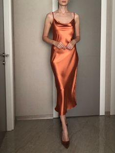 a woman in an orange dress standing next to a door with her hands on her hips