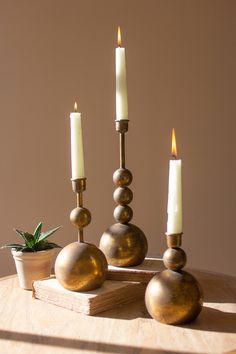 three candles sitting on top of a wooden table next to a potted plant and candle holder