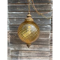 a gold colored glass light hanging from a chain on a wooden wall with wood planks behind it