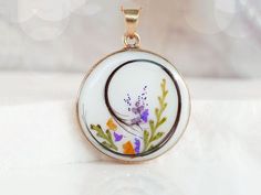 a pendant with flowers painted on it sitting on a white tablecloth covered surface in front of a blurry background