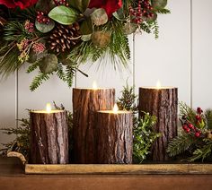 three candles sitting on top of a wooden table next to christmas greenery and pine cones