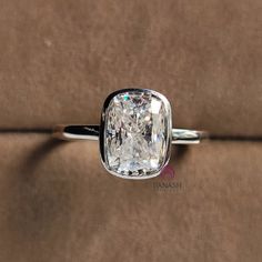 a cushion cut diamond sits on top of a velvet surface in an elegant ring setting