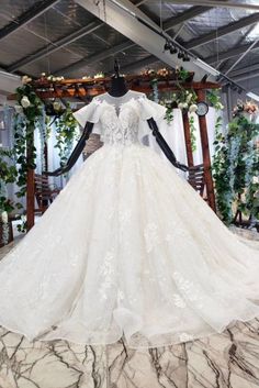 a white wedding dress on display in front of a wooden structure with flowers and greenery