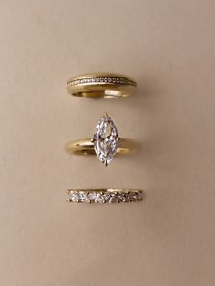 three different types of wedding rings on a beige surface with one diamond in the middle