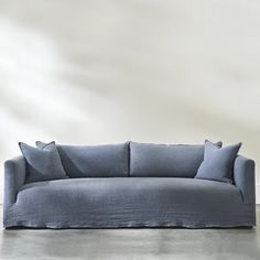 a blue couch sitting on top of a cement floor next to a white wall with two pillows