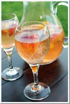 two glasses filled with liquid sitting on top of a wooden table next to a pitcher