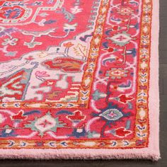 a pink rug with an ornate design on the top and bottom, sitting on a wooden floor