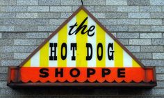 the hot dog shoppe sign is hanging from the side of a brick building with yellow and red stripes