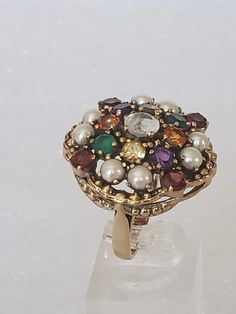 "I'm excited to have come across this beautiful ring because it is in a bigger size and has lots of jewels. The metal is gold plated with a large undercarriage with holes. Each stone is prong set and are in different colored gemstones. The ring has a hallmark \"NB NICKY BUTLER\" and has its original ring box. All stones are intact with non-missing. The ring was used a couple of times and then put away. The finish is shiny with no scratches or other oddities. Makes a great cocktail ring for the H Heirloom Multicolor Ring Jewelry, Vintage Multi-stone Jewelry For Gifts, Oval Jeweled Ring For Gift, Heirloom Multi-stone Cluster Ring, Oval Jeweled Rings For Gifts, Oval Jeweled Rings Perfect For Gifts, Victorian Style Multicolor Jewelry Gift, Antique Multi-stone Cluster Jewelry, Antique Cluster Ring With Gemstone For Gift