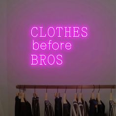 there is a neon sign that says clothes before bros on the wall above some shirts