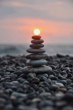 a stack of rocks sitting on top of a beach next to the ocean at sunset