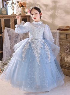 Behold the enchanting allure of our Crystal Blue Flower Girl Dress, meticulously designed to bring fairy-tale dreams to life. This exquisite gown features a stunning high-neck bodice adorned with intricate silver embroidery that cascades down, creating a mesmerizing pattern. Puffy long sleeves add a regal touch, perfect for any elegant, traditional, or bohemian wedding theme. The multi-layered tulle skirt, dusted with delicate sparkles, flows gracefully with every step, ensuring your flower girl feels like a princess. The dress is designed to offer both comfort and style, allowing her to move freely and confidently. Whether she is walking down the aisle or twirling on the dance floor, this gown will make her radiate pure charm and grace. Elevate her role in your special day with this breat Long Sleeve Flower Girl Dress, Blue Flower Girl Dress, Bohemian Wedding Theme, Custom Made Wedding Dresses, Blue Flower Girl, Flower Girl Dresses Blue, Classic Glamour, Sparkle Skirt, Prom Look