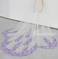 a veil with purple flowers on it is hanging from the ceiling in front of a mannequin