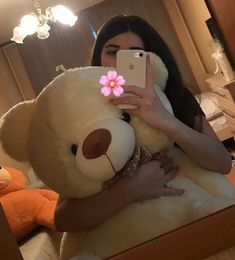 a woman taking a selfie with her phone and holding a large stuffed teddy bear