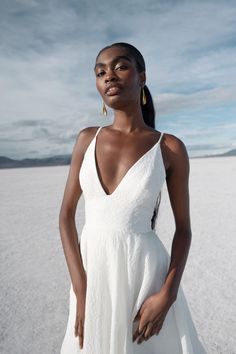 a woman in a white dress standing on the sand with her hands behind her back