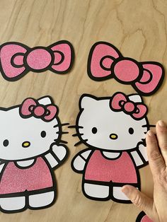 hello kitty cutouts are being held up by someone's hand on a wooden surface