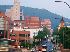 a city street filled with lots of traffic next to tall buildings and green hills in the background