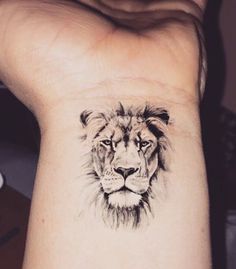 a small tattoo on the wrist of a woman with a lion head in black ink