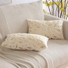 two white pillows sitting on top of a couch next to a vase with yellow flowers