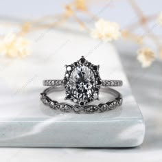 an oval cut engagement ring with black diamond accents on a white marble surface next to flowers