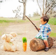 a little boy sitting on top of a log next to a teddy bear and carrot