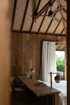 a bed sitting under a ceiling fan next to a wooden table with chairs around it