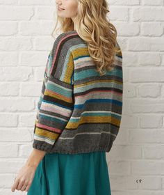 a woman standing in front of a white brick wall wearing a multicolored sweater