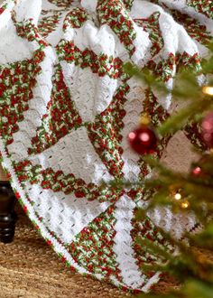 a white crocheted blanket with red and green flowers on it next to a christmas tree