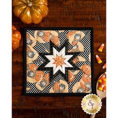 an orange and black quilt on a wooden table with candy in the foreground, pumpkins behind it