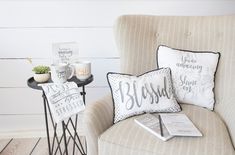 a chair with two pillows on top of it next to a side table and coffee cup