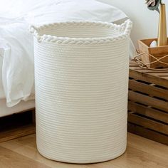 a large white basket sitting on top of a wooden floor next to a bed in a bedroom