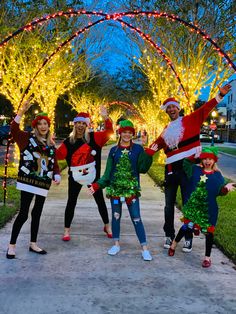 group of people dressed up for christmas posing in front of trees with lights on them