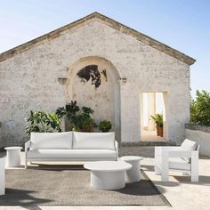 an outdoor living area with white furniture and potted plants on the side of the building