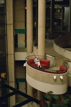 a man sitting in a red chair on top of a circular bench next to a tall building