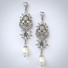 A classy pair of bridal earrings in art deco vintage inspired style. The flawlessly faceted cubic zirconia stones capture the light in a dazzling array of sparkles, while the delicate white pearls add fluidity and motion. The earrings are rhodium / rose gold / yellow gold plated for a bright finish which enhances the intricate detailing and conveys a modern take on old elegance. Length 2.5" (approx. 6.3cm); Width: 0.6" (approx. 1.5cm); Weight: 4.9g Available in Silver, Rose Gold and Yellow Gold Elegant Cubic Zirconia Bridal Earrings For Evening, Elegant Bridal Earrings In Diamond White Cubic Zirconia, Glamorous Sterling Silver Wedding Chandelier Earrings, Glamorous Sterling Silver Chandelier Earrings For Wedding, Elegant Diamond White Crystal Earrings With Sparkling Stones, Wedding Chandelier Earrings With Diamond Accents In Cubic Zirconia, Elegant Diamond White Cubic Zirconia Chandelier Earrings, Wedding Chandelier Earrings With Diamond Accents And Cubic Zirconia, Wedding Chandelier Earrings With Cubic Zirconia And Diamond Accents