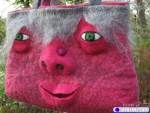 a pink bag with green eyes is hanging from a tree in front of the camera