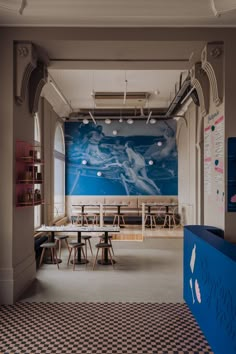 an empty room with tables and chairs in front of a large mural on the wall