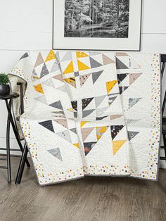 a quilted blanket sitting on top of a wooden floor next to a chair and potted plant