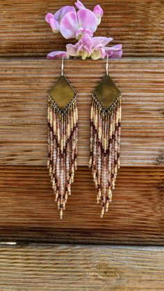 two brown and white earrings hanging from a wooden wall next to pink orchids on the side