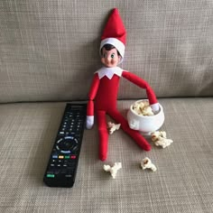 an elf is sitting on the couch next to a remote control and bowl of popcorn